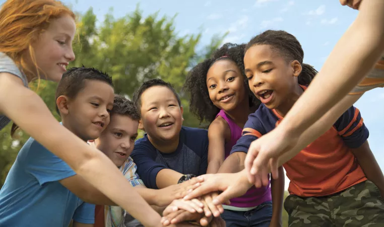 A group of kids putting their hands together for a cheer. 