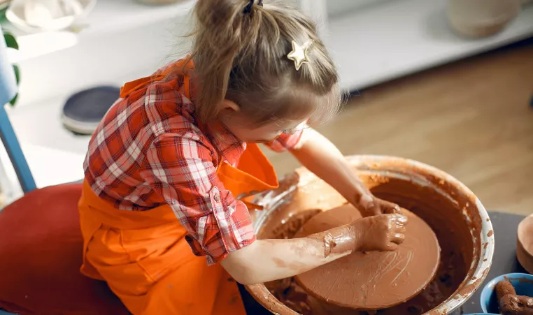 Young child sits at a pottery wheel working with clay. 