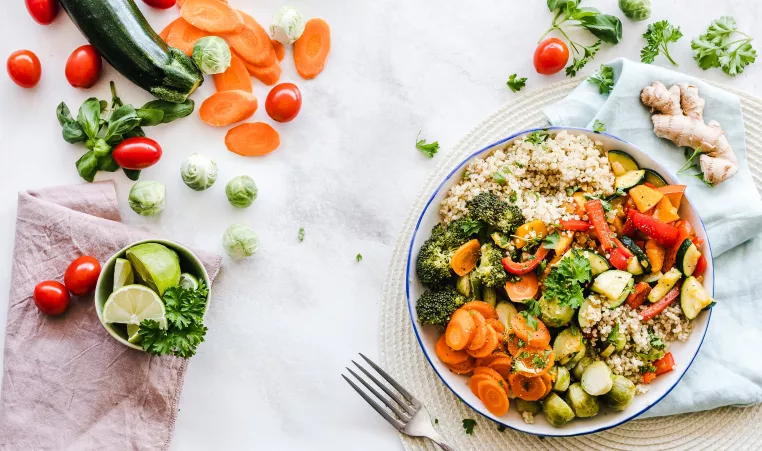 A vegetable salad with steamed broccoli, carrots, and zucchini ona. anice table with other vegetables spread anpoit