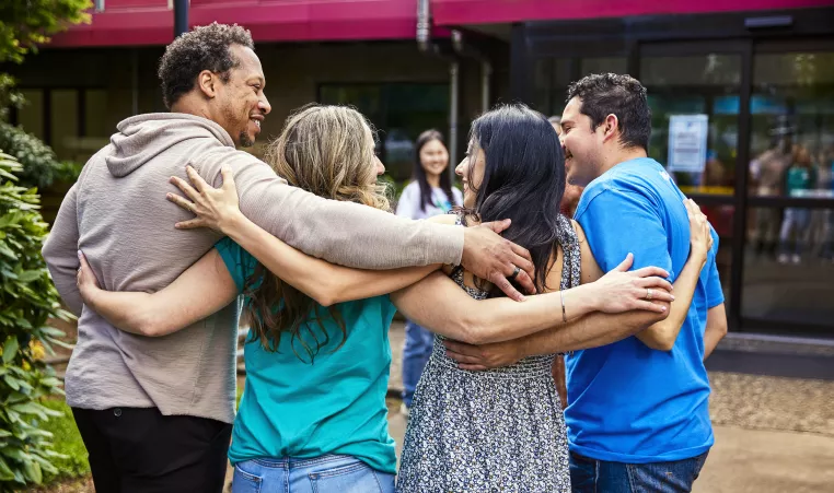 A group of four adults hugging and smiling